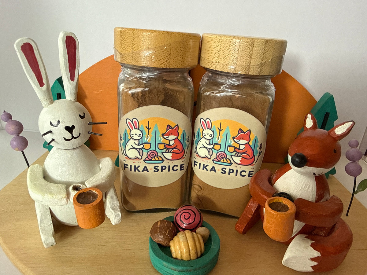 Two jars of 'Fika Spice' with animal figurines and decorative items on a wooden surface.