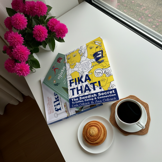 At-home fika scene with black coffee, pastry, flowers, and a book about Swedish fika