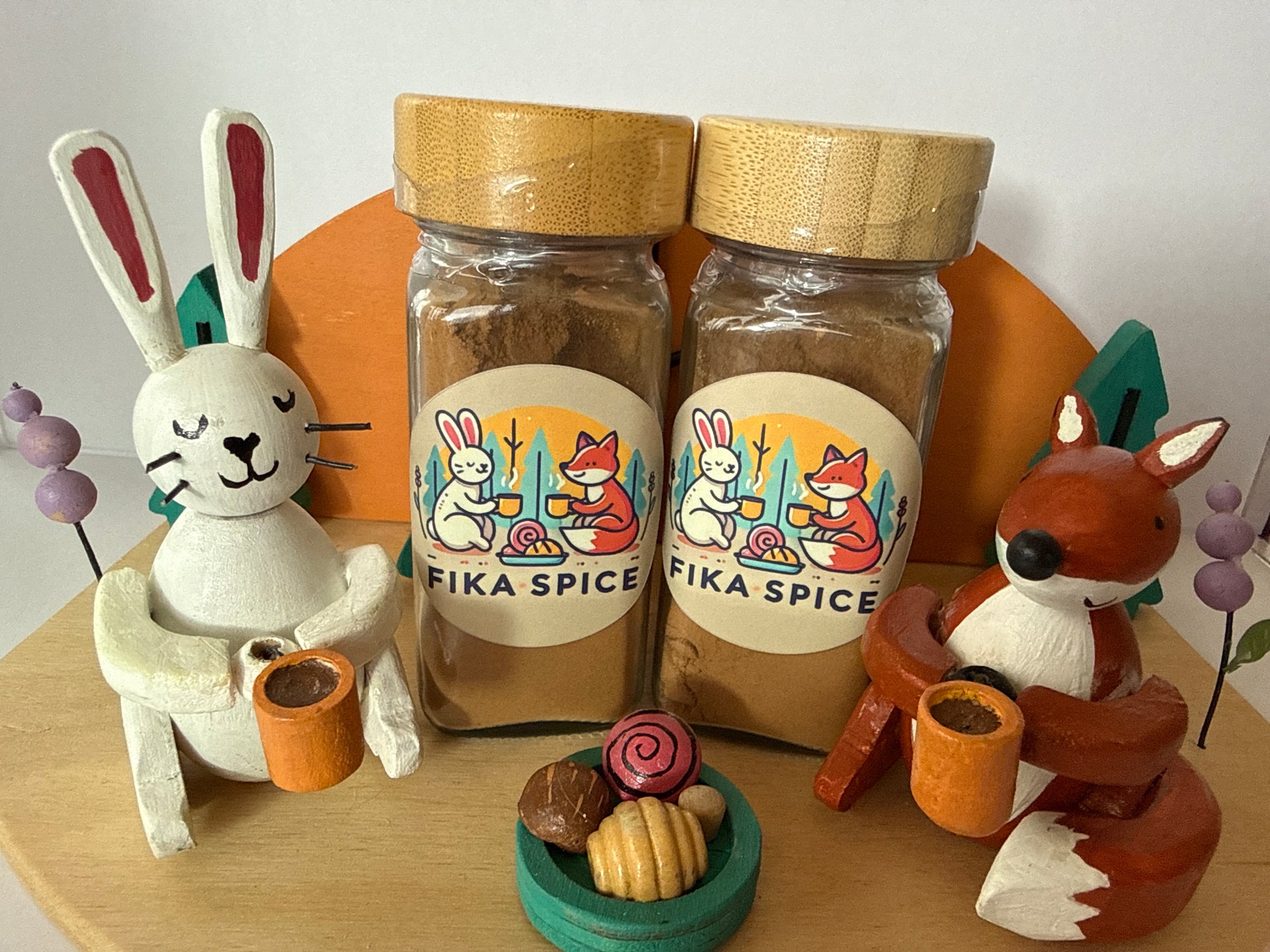 Two jars of 'Fika Spice' with animal figurines and decorative items on a wooden surface.