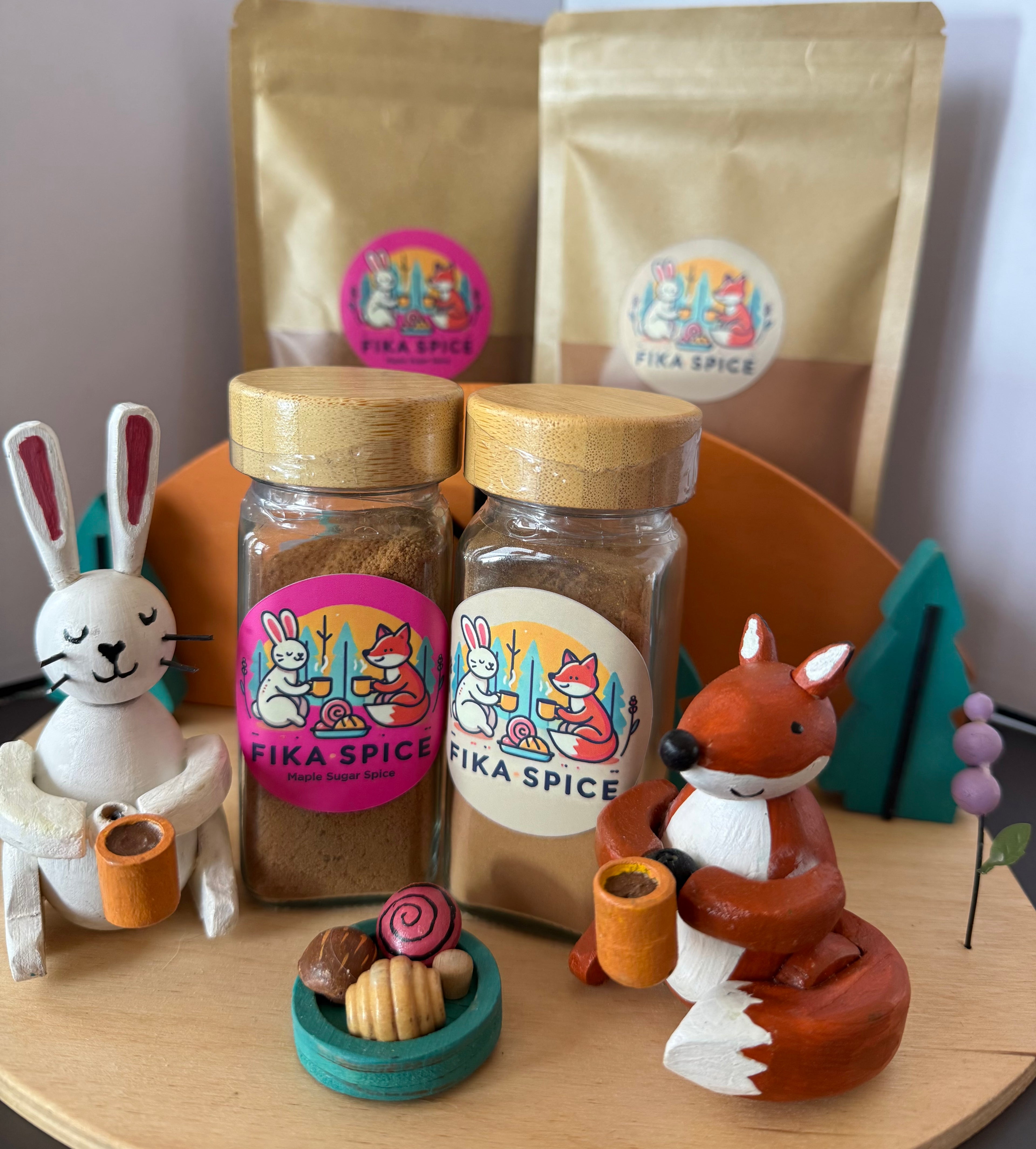 Two jars of Fika Spice with decorative animal figures and packaging on a wooden surface having a luxurious Fika with coffee and pastries, slowing down, relaxing as a Fika should be.