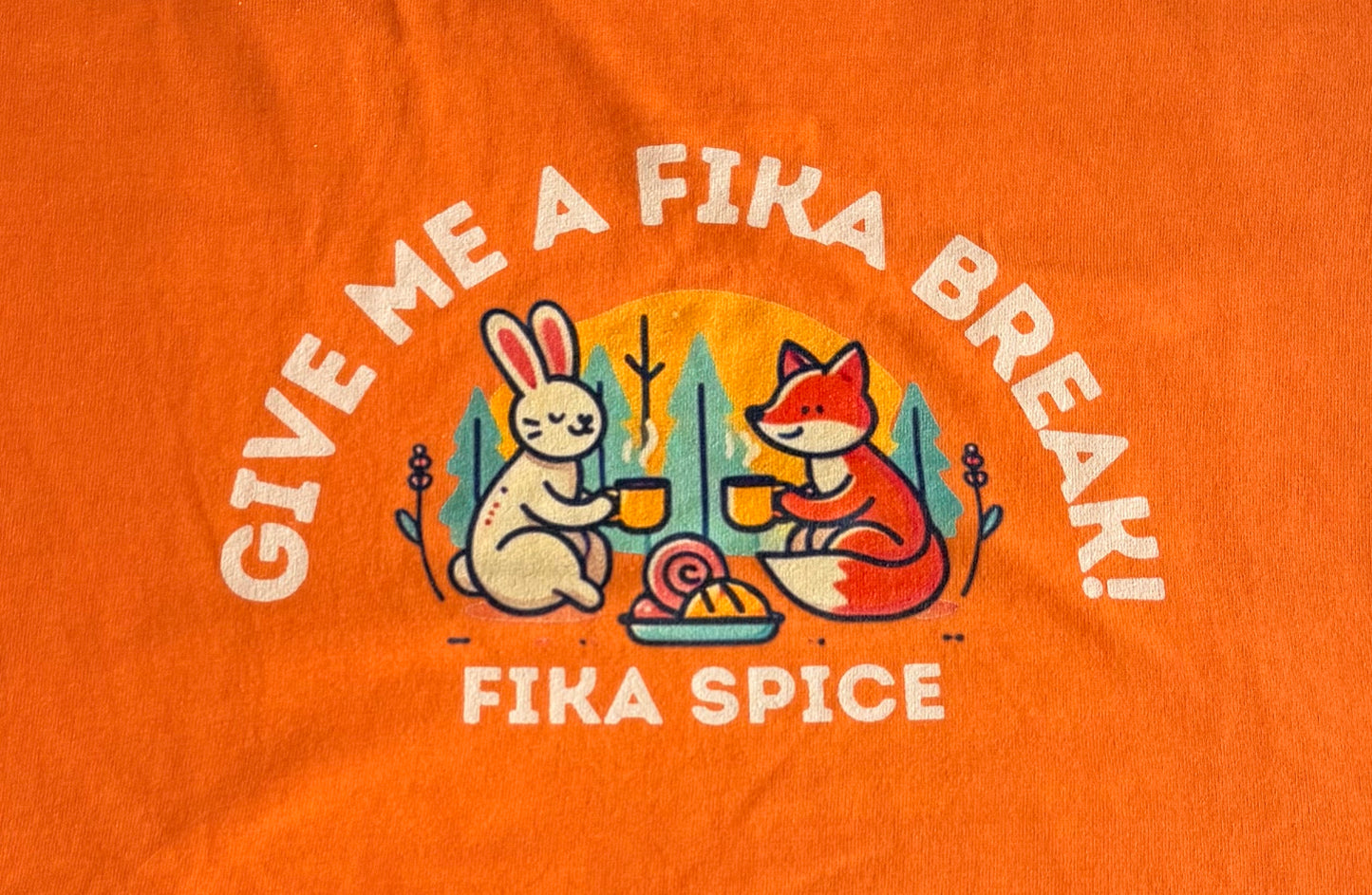 Orange t-shirt with cartoon fox and rabbit design and text 'Give Me A Fika Break! Fika Spice' on an orange background. Fika Spice Scandinavian coffee spice blend with cinnamon and cardamom crated with antioxidant-rich spices for a daily healthy treat.