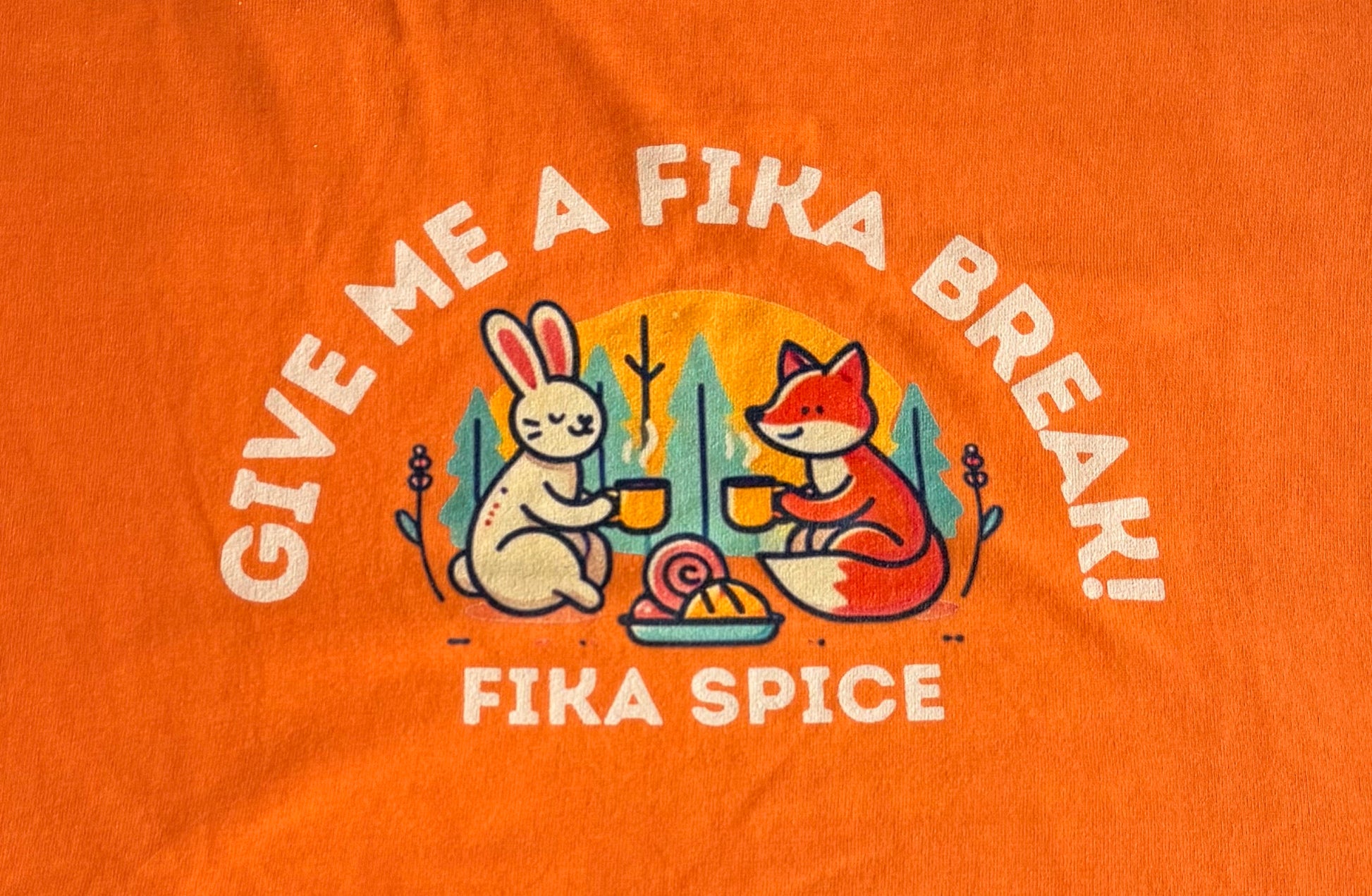 Orange t-shirt with cartoon fox and rabbit design and text 'Give Me A Fika Break! Fika Spice' on an orange background. Fika Spice Scandinavian coffee spice blend with cinnamon and cardamom crated with antioxidant-rich spices for a daily healthy treat.